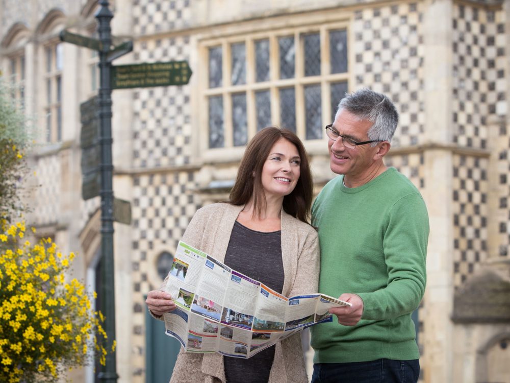 A woman sat on a coach looking at the camera, wearing a hat and sunglasses.