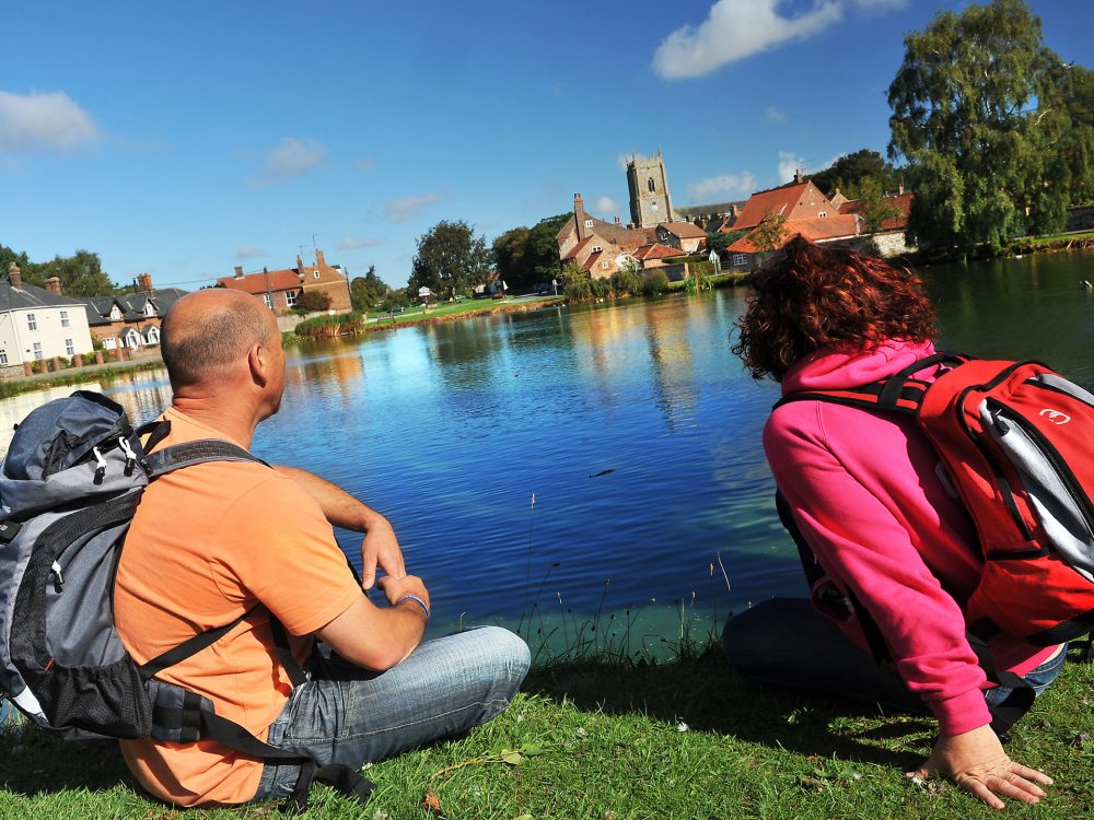 A couple overlooking Great Massingham village wearing back packs on their shoulders.