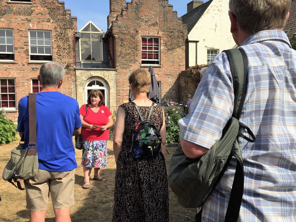 A couple standing in front of King's Lynn Town Hall holding a Discover King's Lynn leaflet. The man is wearing a green jumper and the woman is wearing a beige cardigan.