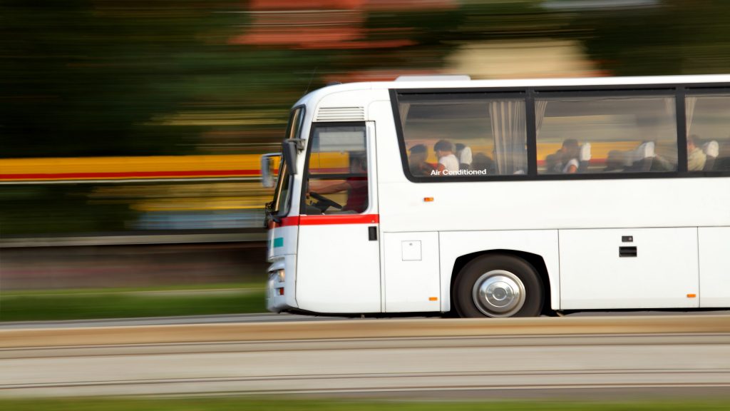 A white coach driving down the road at a fast speed. The bus has a sign that states "Air Conditioned" on a window.