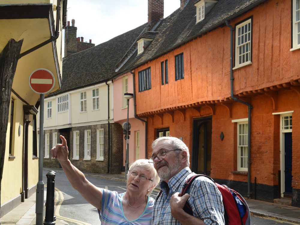A woman sat on a coach looking at the camera, wearing a hat and sunglasses.