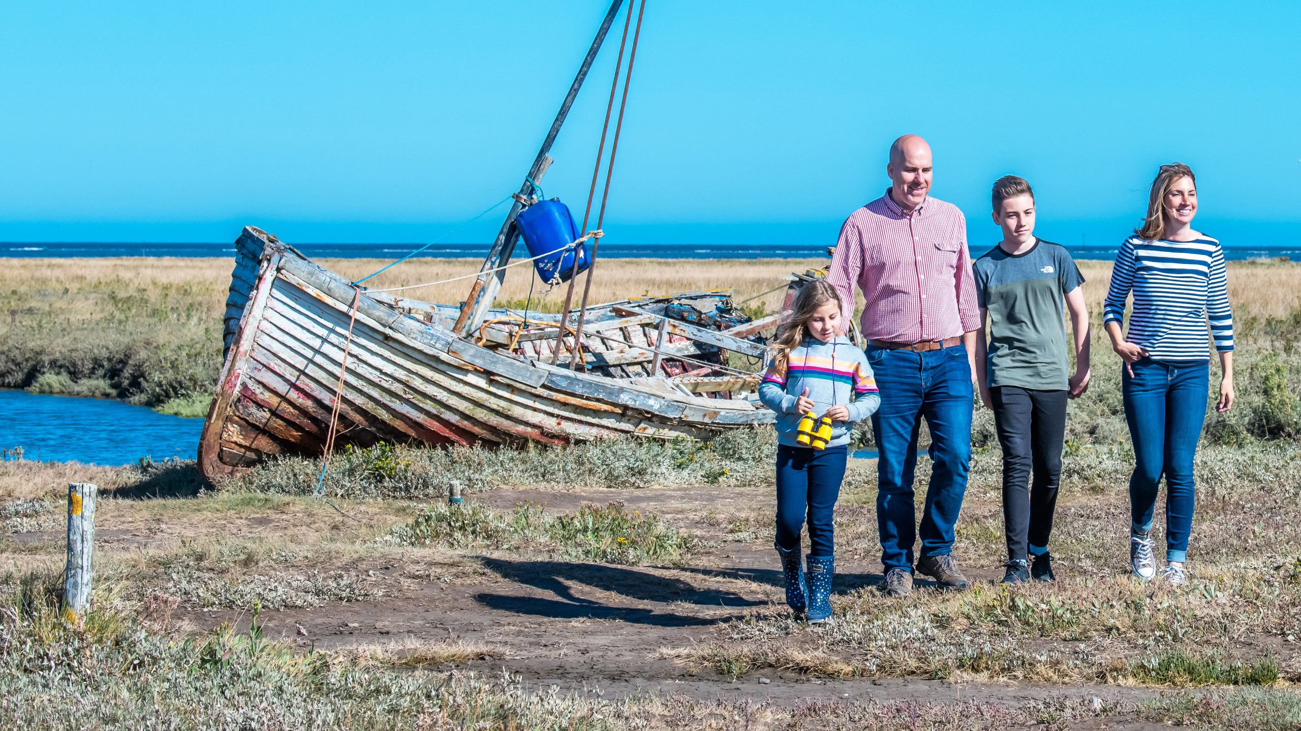 A family of four walking away from the wreck of a boat in Burnham Overy Staithe.