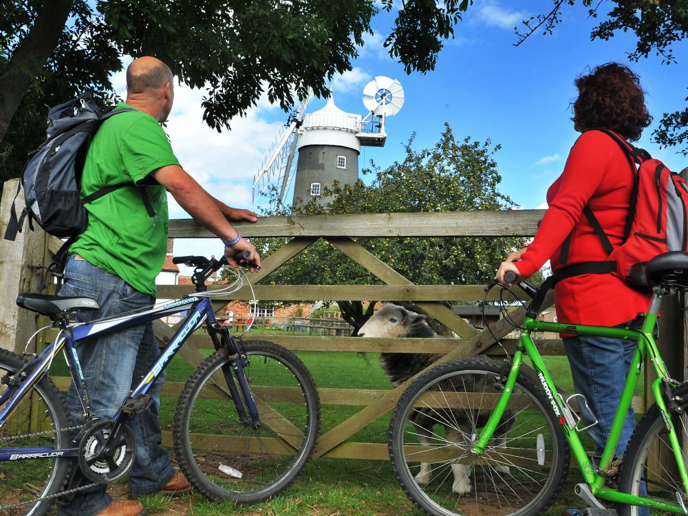 A couple standing and holding their bikes whilst looking over at Bircham Windmill.