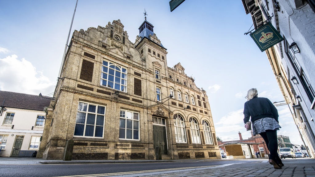 A below shot of Downham Market Town Hall with a woman walking past.