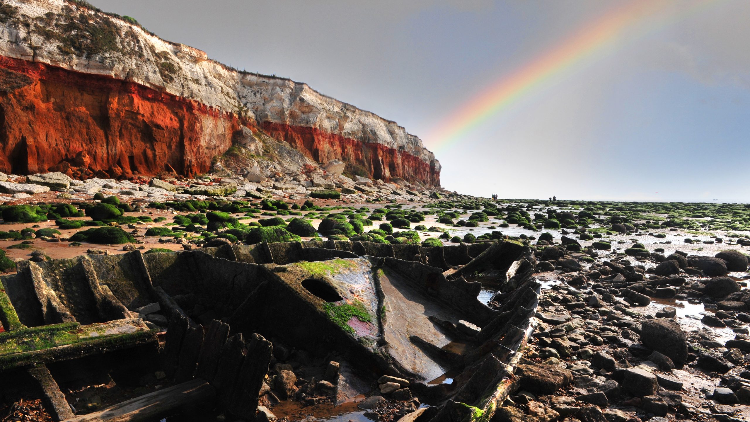 The red and white striped cliffs at Old Hunstanton beach with a rainbow in the sky.
