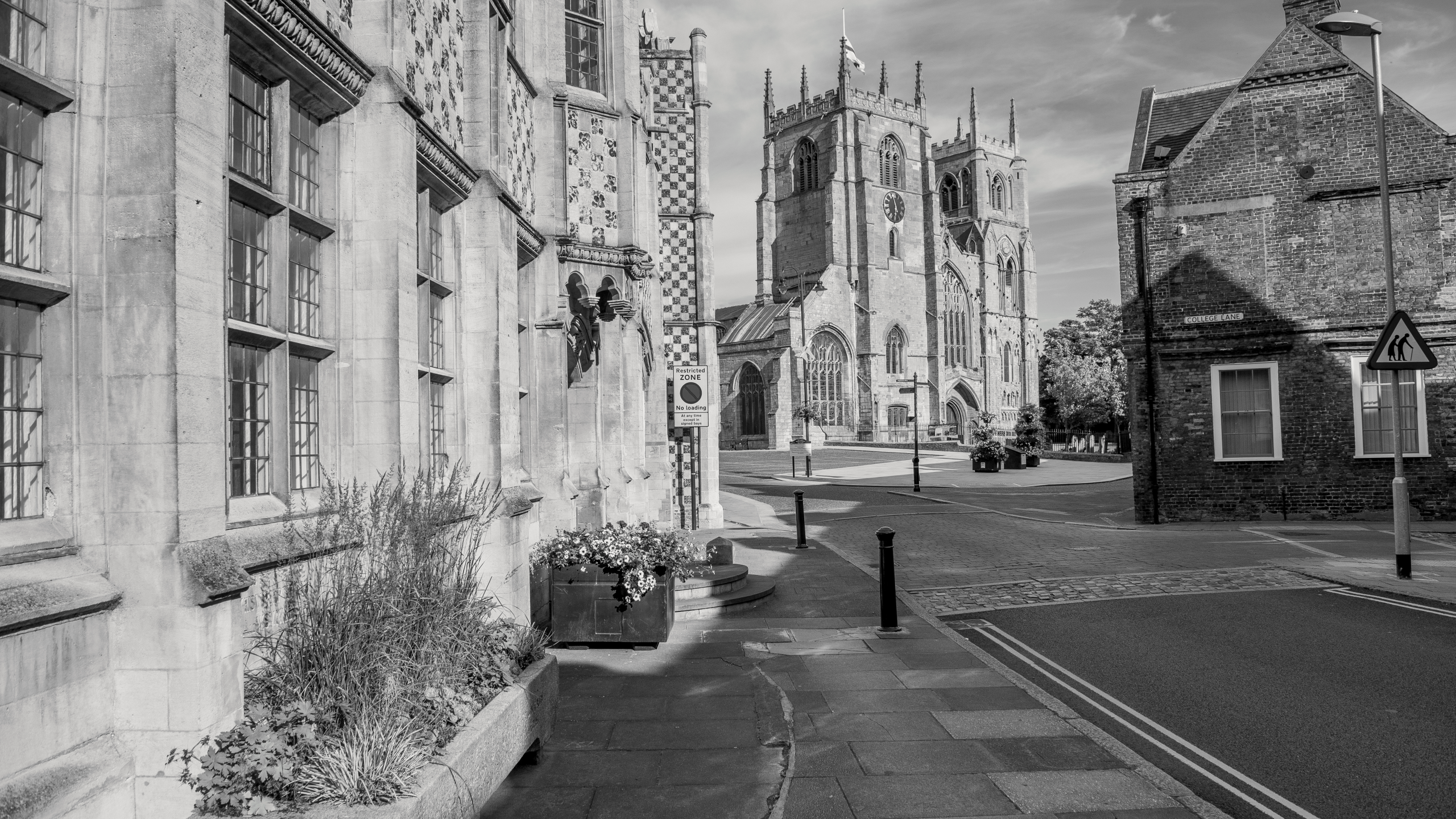 A black and white image of Saturday Market Place in King's Lynn. To the left of the image is the chequered King's Lynn Town Hall and in the background is King's Lynn Minster.