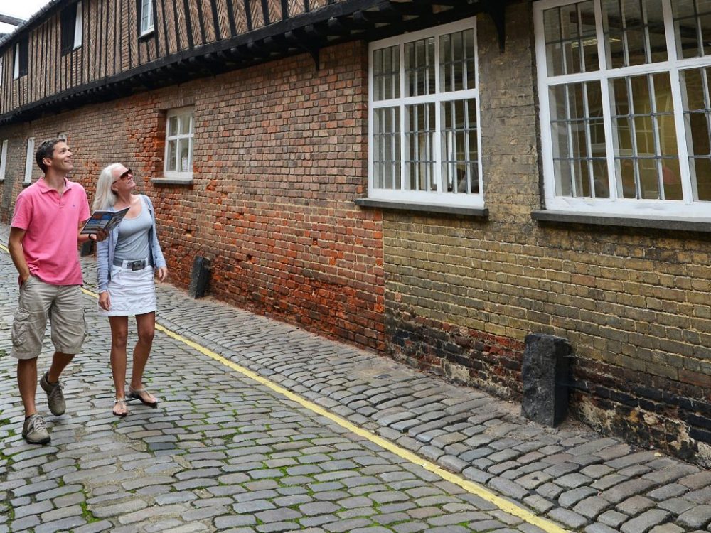 A couple standing in front of King's Lynn Town Hall holding a Discover King's Lynn leaflet. The man is wearing a green jumper and the woman is wearing a beige cardigan.