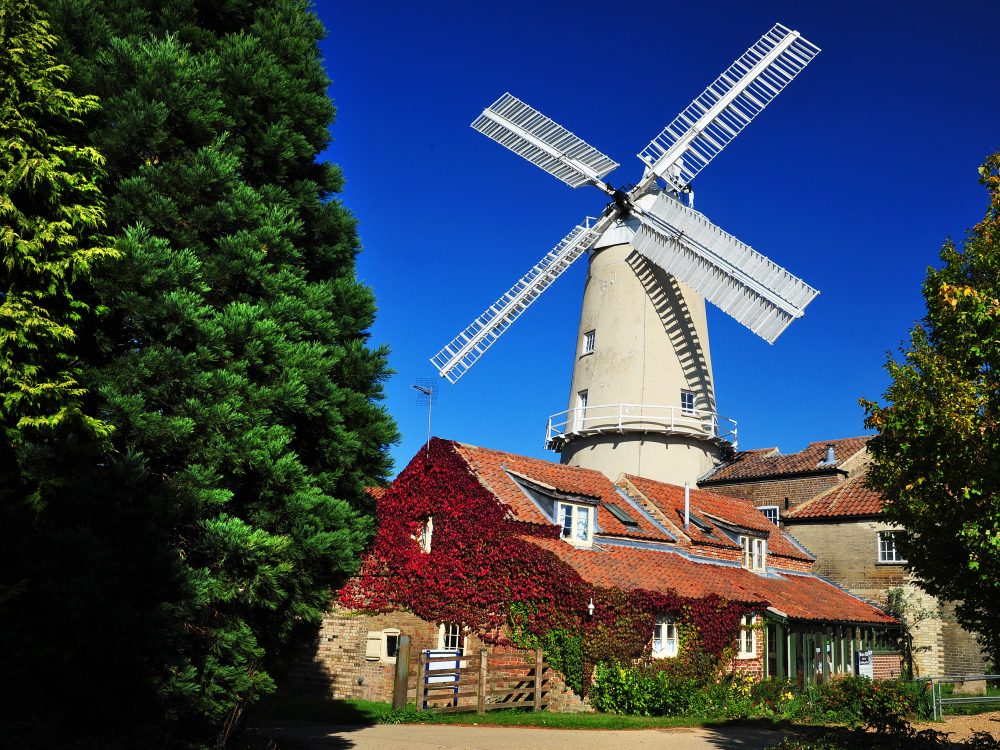 An elderly couple holding their bikes and looking over Castle Rising Castle.