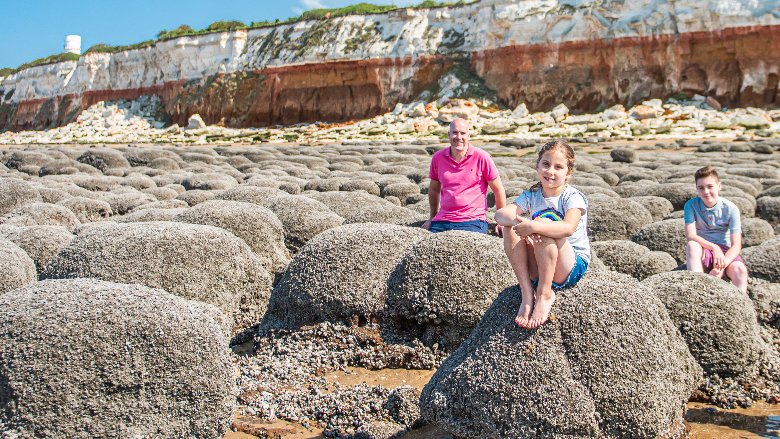 A family of three sitting on the rocks near the beach at Old Hunstanton