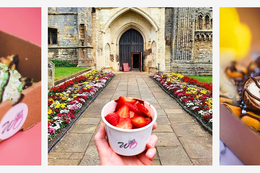A happy shot of a family of four walking away from a village store. From left to right, a young boy is smiling at the camera wearing a short sleeved t-shirt and black jeans. An older man is standing in the middle of the image wearing a pink shirt and blue jeans. He is holding the hand of a little girl wearing a bright pink long sleeved t-shirt smiling. The little girl is also holding the hand of a woman who is smiling and wearing a striped long sleeved t-shirt and jeans.