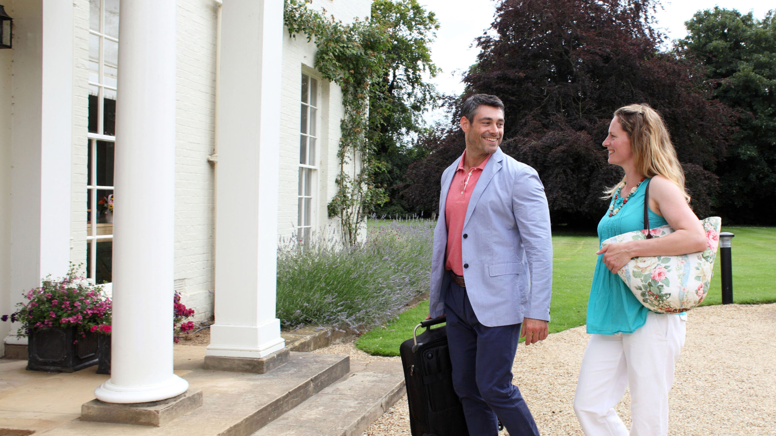 A couple walking towards a hotel holding a suitcase and travel bag