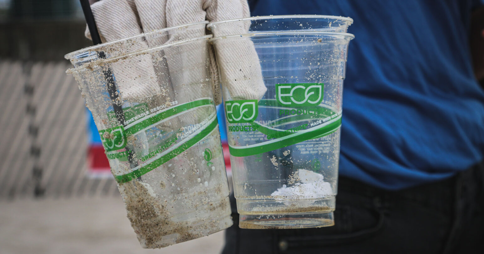 A person holding two littered plastic cups with the term 'ECO' on them