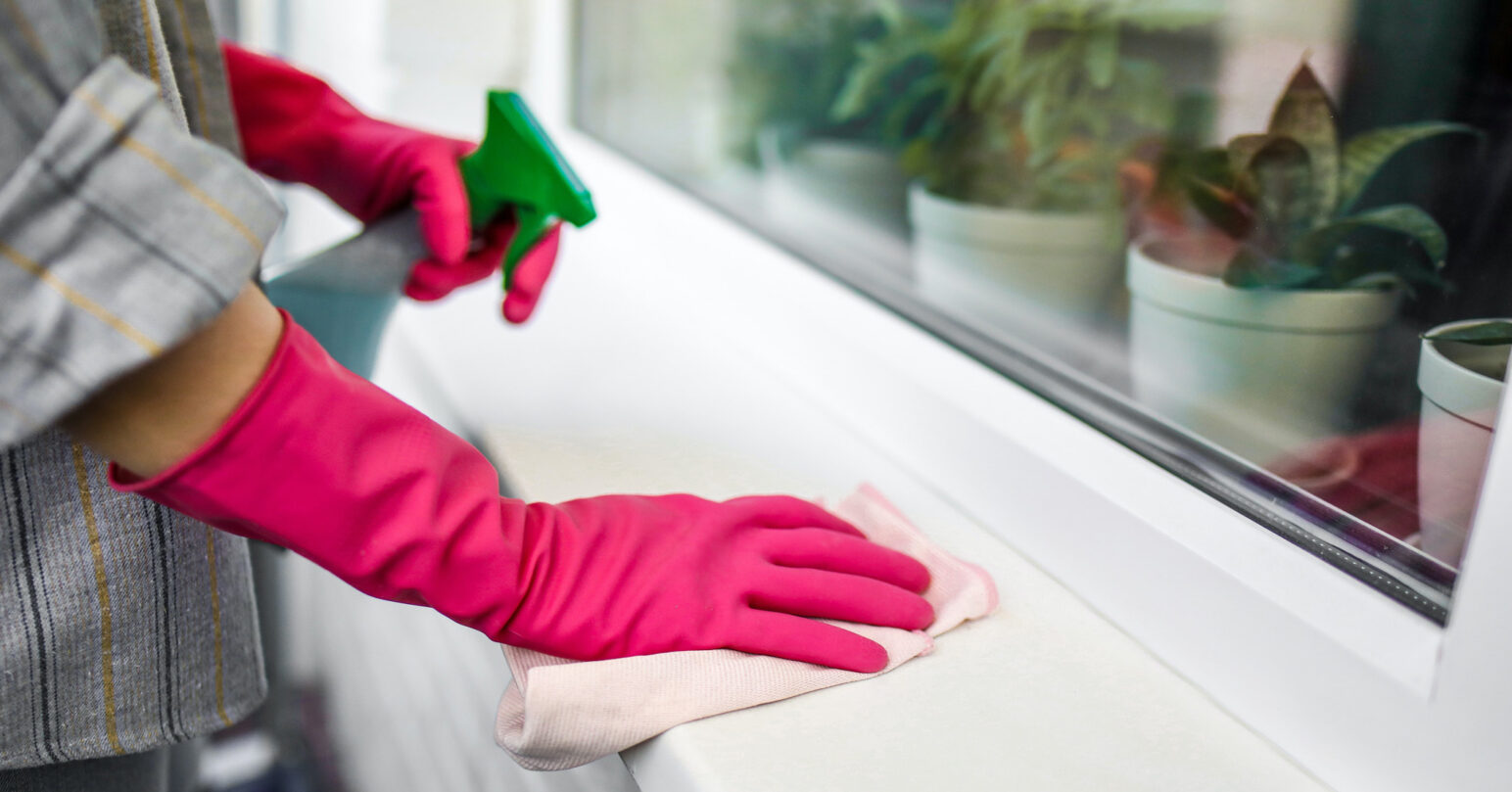 A person cleaning a windowsill using eco-friendly cleaning products and pink rubber gloves