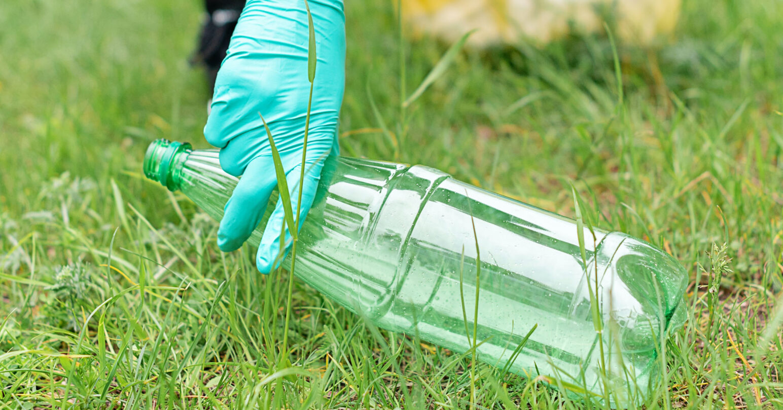A person picking up a plastic bottle wearing a rubber glove