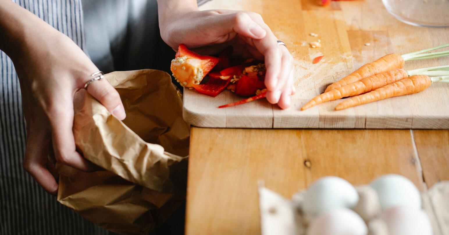 A person pushing food scraps into a paper bag from a wooden board