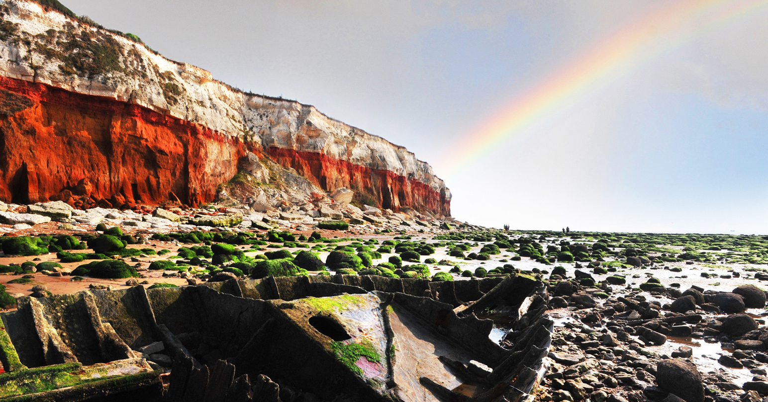 The red and white striped cliffs at Old Hunstanton beach with a rainbow in the sky.