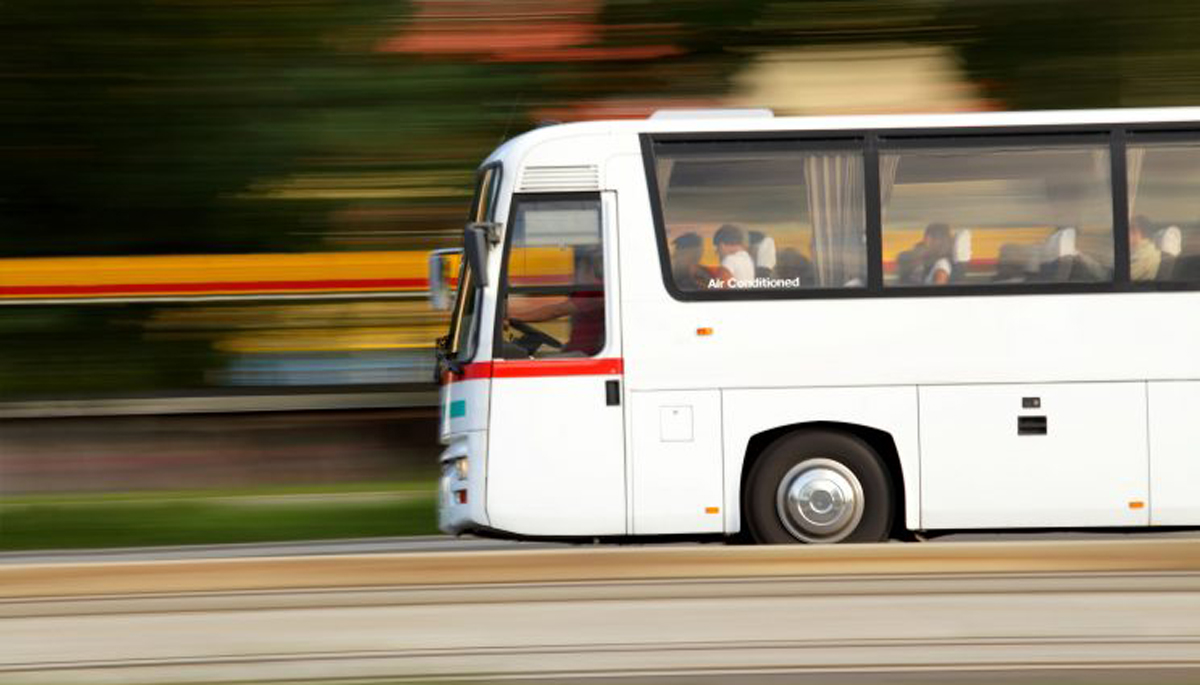 A white coach driving down the road at a fast speed. The bus has a sign that states "Air Conditioned" on a window.