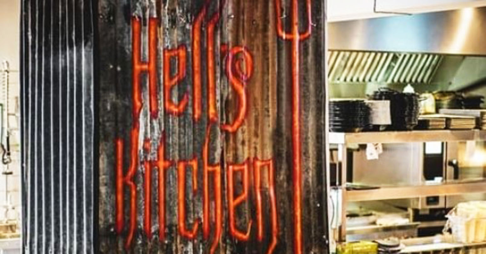 The interior of Liquor and Loaded in King's Lynn. The words "Hell's Kitchen" with a cartoon pitchfork is painted on the wall next to the kitchen area.