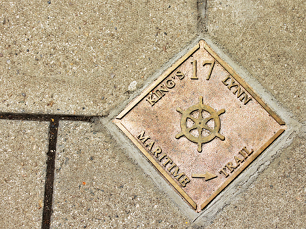 A plaque on the ground that says "King's Lynn 17 Maritime Trail" with an arrow that guides visitors around the trail.
