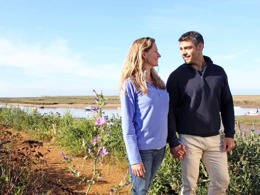 A couple looking through a hide and holding binoculars at RSPB Titchwell Marsh Nature Reserve in West Norfolk.