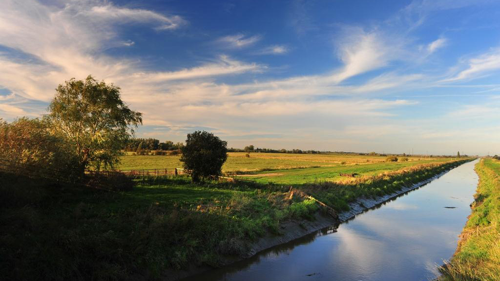 A panoramic shot of a river running through the fens landscape.
