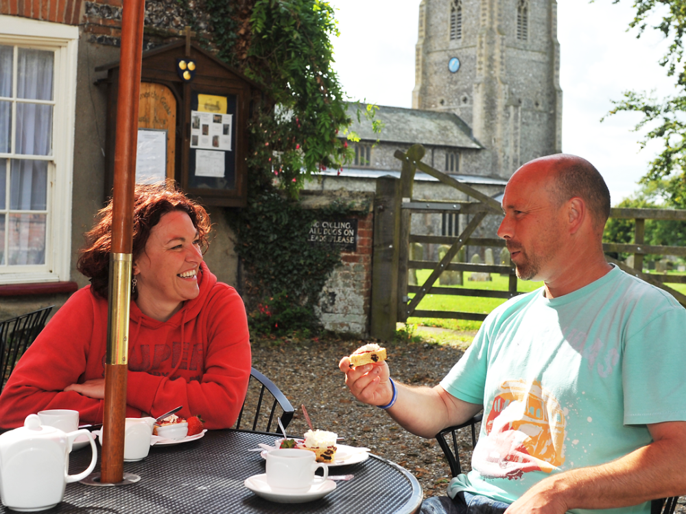 An elderly couple holding their bikes and looking over Castle Rising Castle.