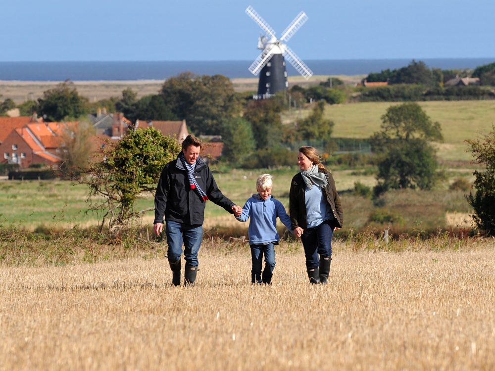 A family of three holding hands and walking through Burnham Overy in West Norfolk.