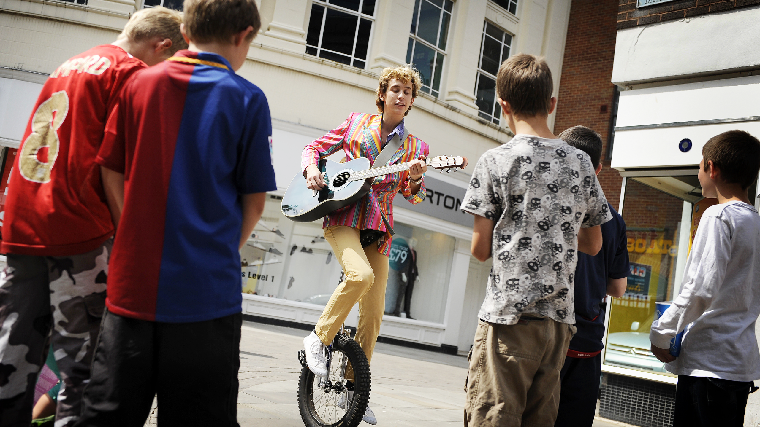 A performer playing guitar on a unicycle in front of a group of young children in King's Lynn, West Norfolk.