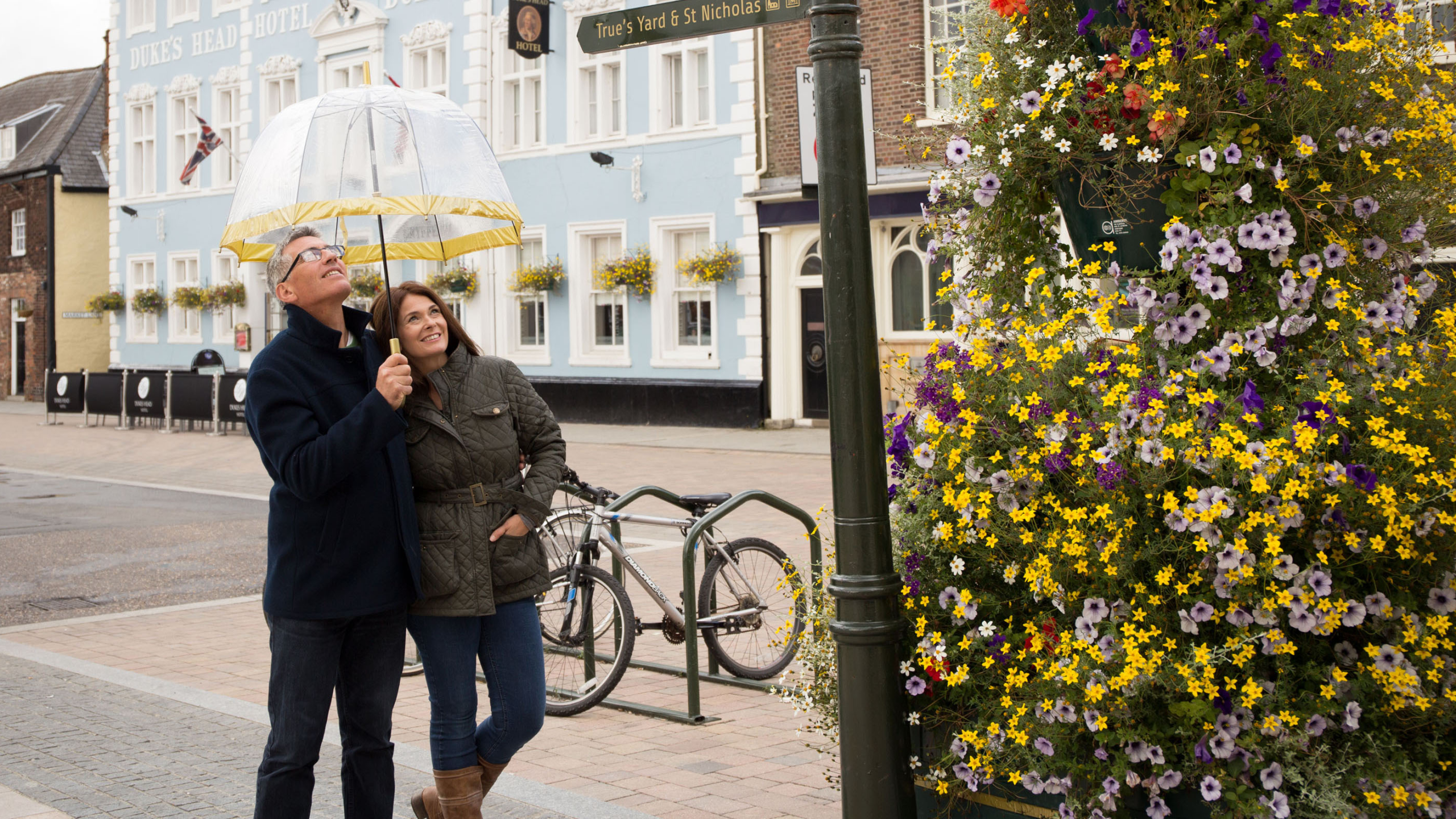 A couple smiling on Tuesday Market Place in King's Lynn holding an umbrella.