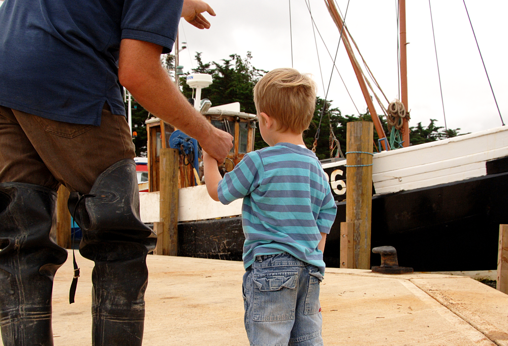 A child looking at a moored fishing boat and holding the hand of an adult in west Norfolk.