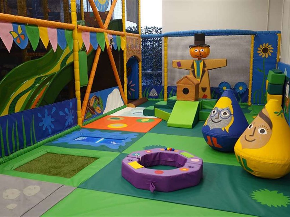A happy shot of a family of four walking away from a village store. From left to right, a young boy is smiling at the camera wearing a short sleeved t-shirt and black jeans. An older man is standing in the middle of the image wearing a pink shirt and blue jeans. He is holding the hand of a little girl wearing a bright pink long sleeved t-shirt smiling. The little girl is also holding the hand of a woman who is smiling and wearing a striped long sleeved t-shirt and jeans.